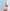 A person in a white robe holds a bottle of Bellamiluxx Body Acne Cleanser against a light blue tiled wall, with soap foam on their leg and bubbles floating around.